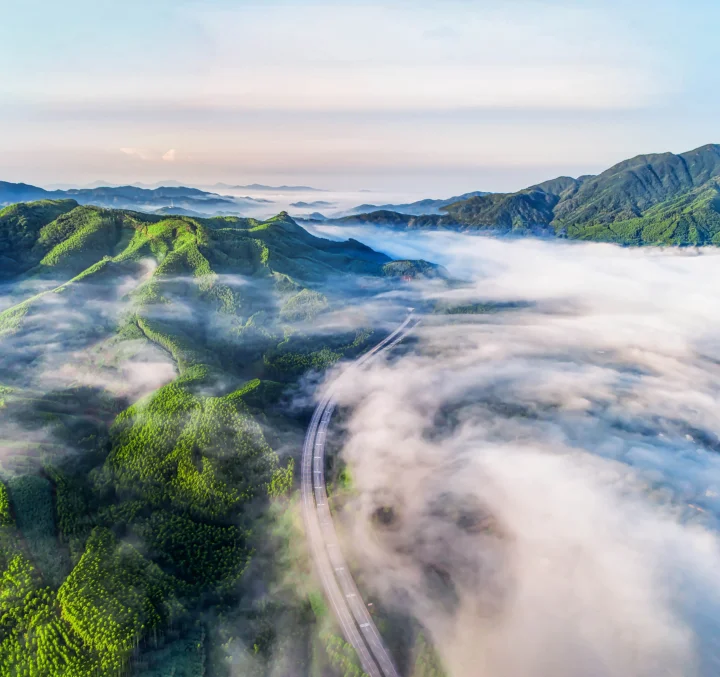 群山與綠色森林被雲霧環繞，一條公路蜿蜒穿過山谷。