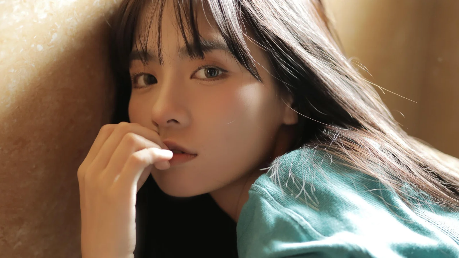긴 머리의 성인 여성이 따뜻한 햇살 속에서 카메라를 바라보며 손가락을 입술에 살짝 대고 있다.