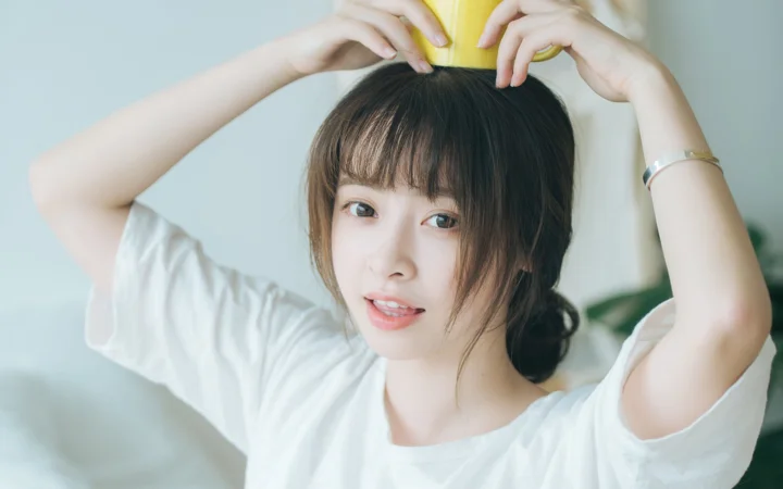 一名身穿白色T恤的女子抬起双臂，双手环绕着头顶的黄色物体。
