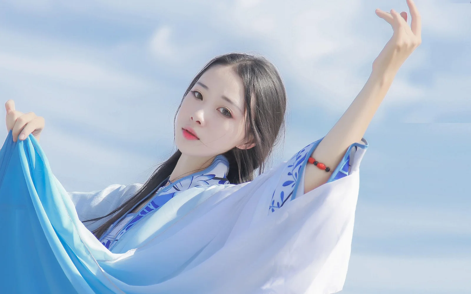 一名身穿蓝白传统服饰的女子在蓝天背景前展开衣袖。