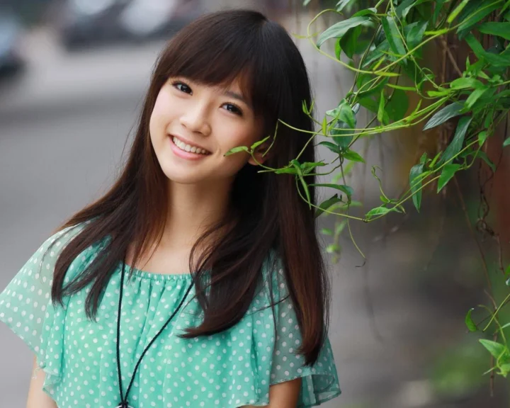 一位身穿绿色波点上衣的成年女性在绿植旁微笑面对镜头。