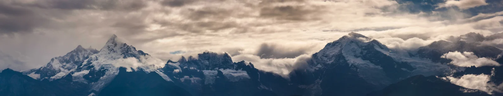壮阔的雪山群峰在厚重云层下延伸成一幅宽屏全景。