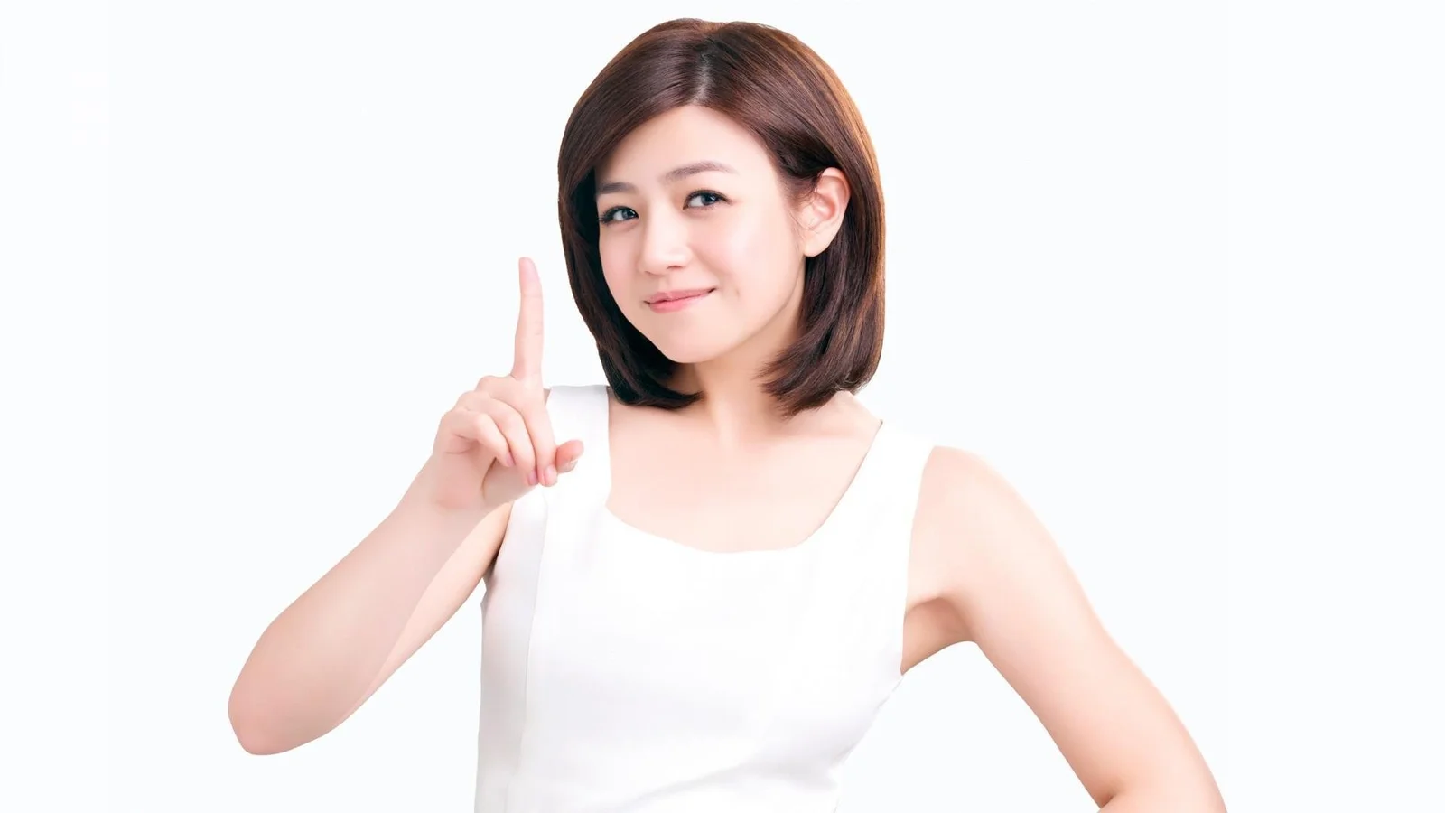 一位短髮女性穿著白色無袖上衣站在白色背景前，抬起手指微笑示意。