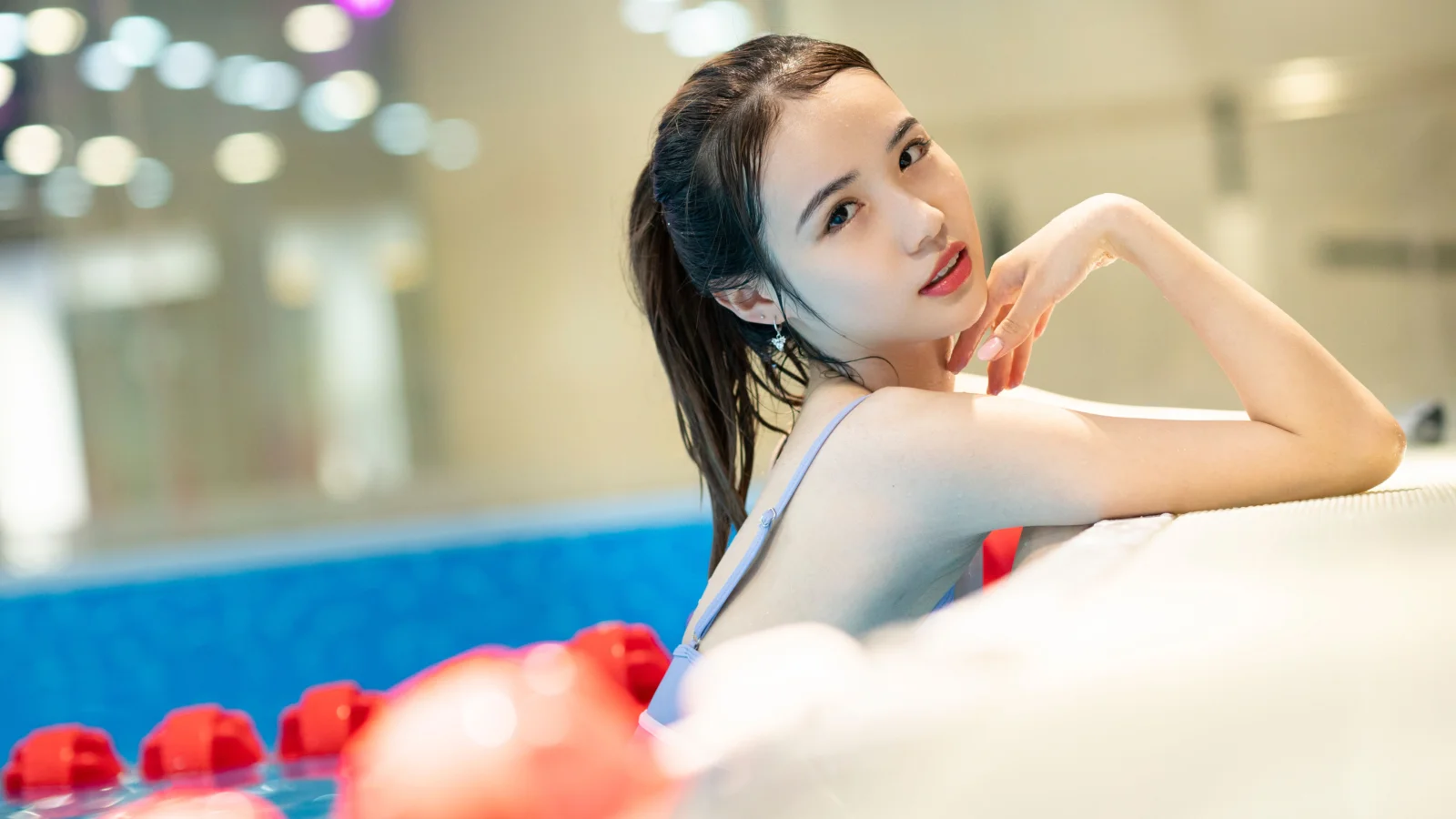 一名女子靠在泳池边，背景呈现柔和的虚化灯光。