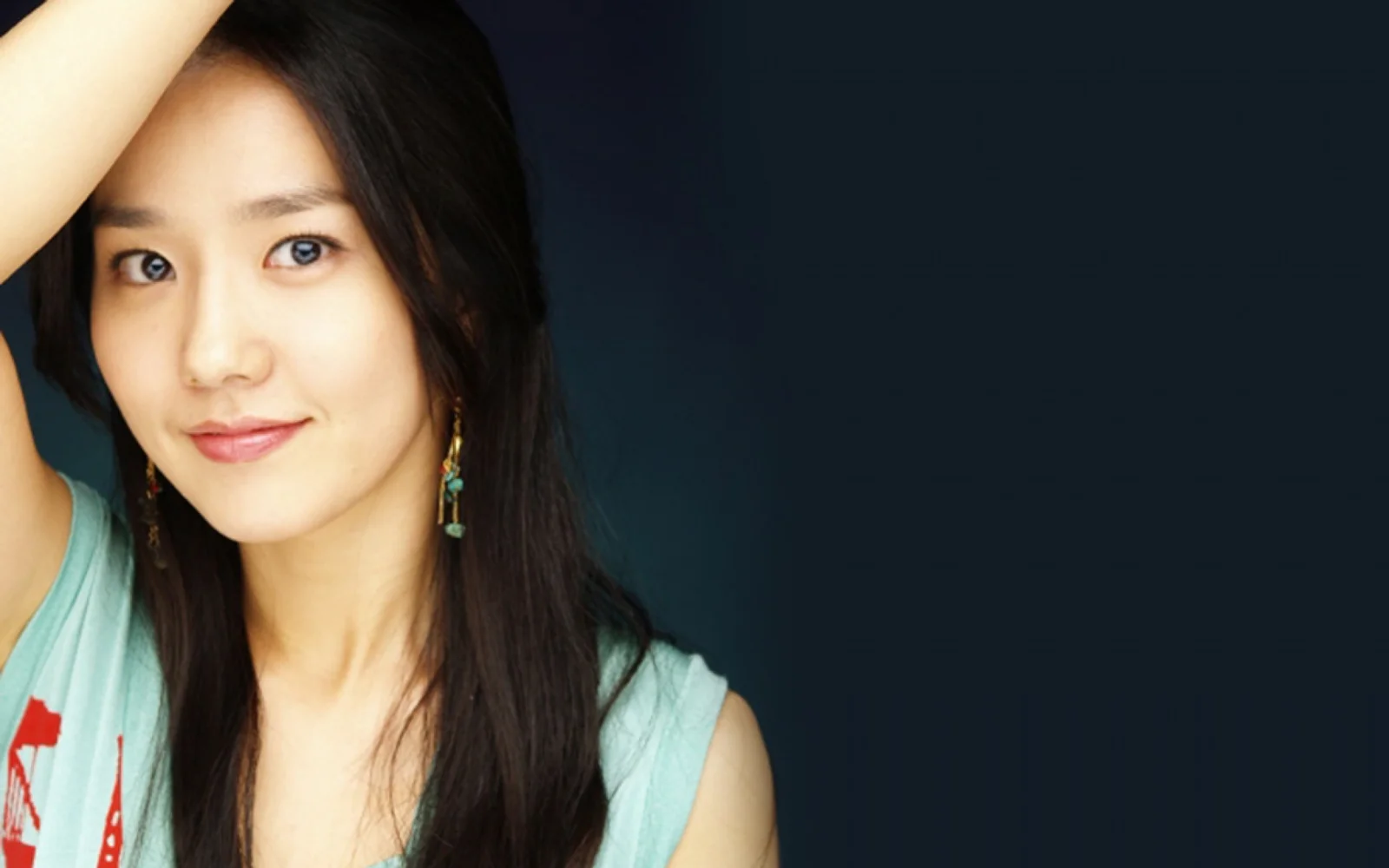 一名长发女性在深色背景前抬起手臂微笑面对镜头。