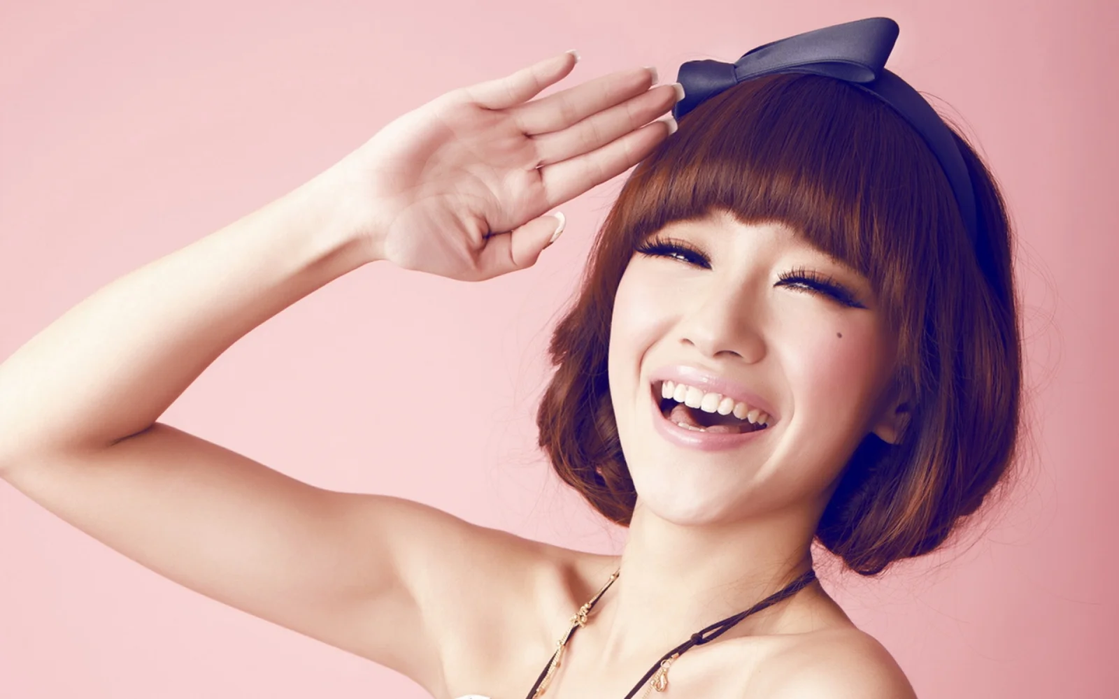 리본 머리 장식을 한 여성이 분홍색 배경 앞에서 미소를 지으며 손을 들고 있습니다.