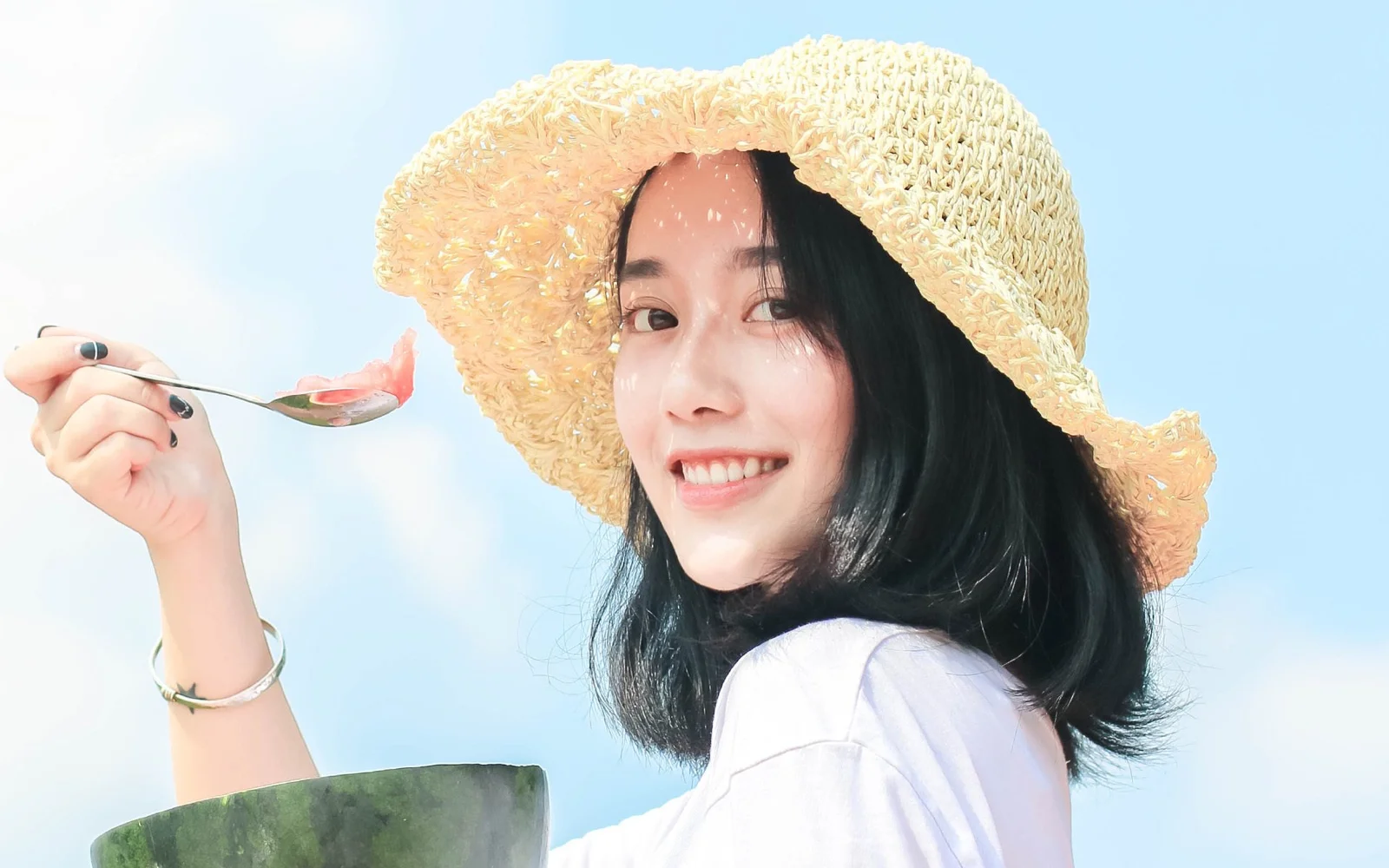 一位戴草帽的女性面带微笑，手持勺子面对镜头。