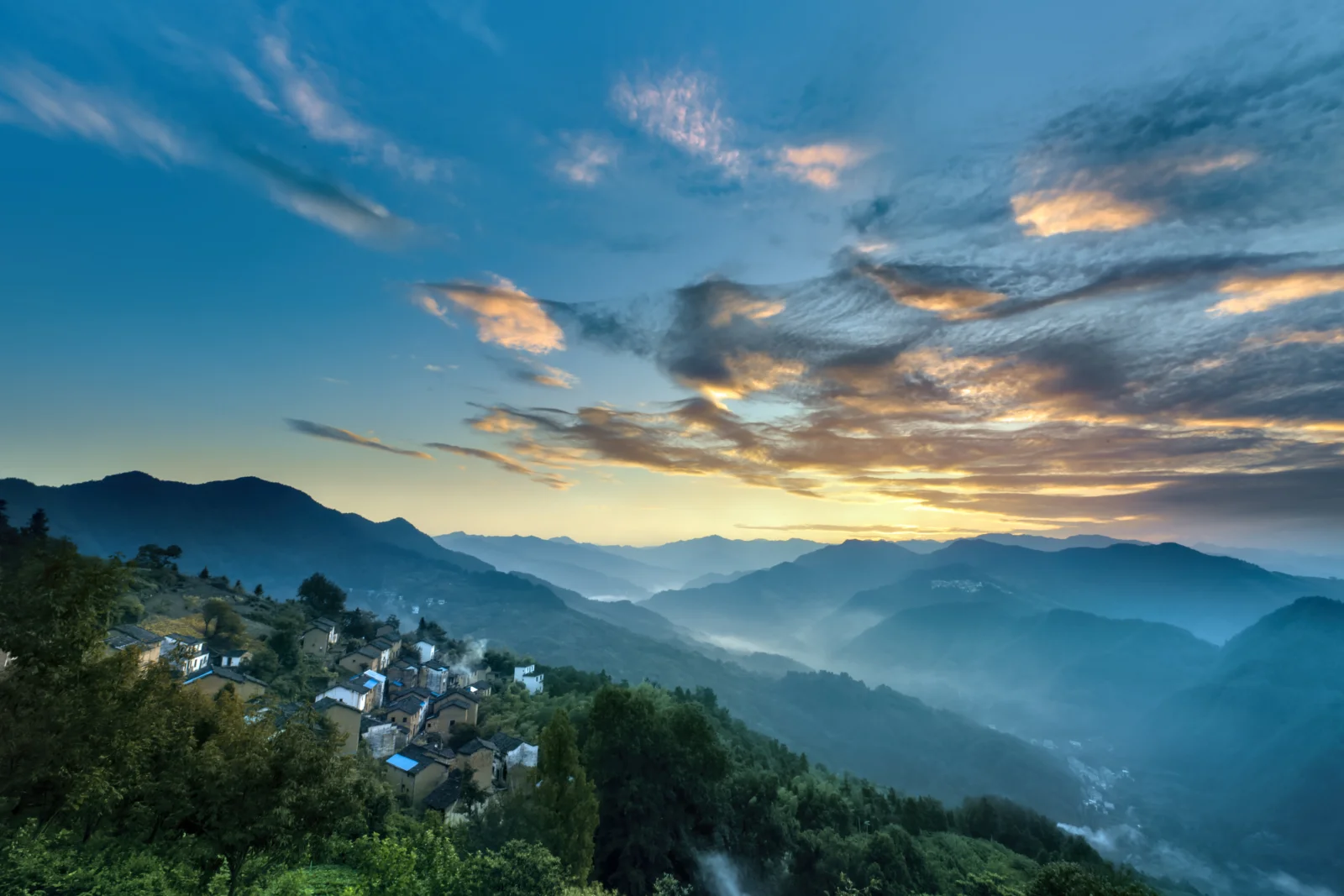夕阳映照下的群山、森林与山间村落构成宁静的自然景色。