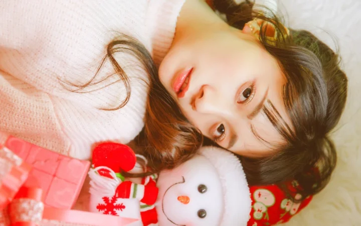 一名女子穿着粉色毛衣躺在浅色背景上，身旁抱着一只雪人玩偶。