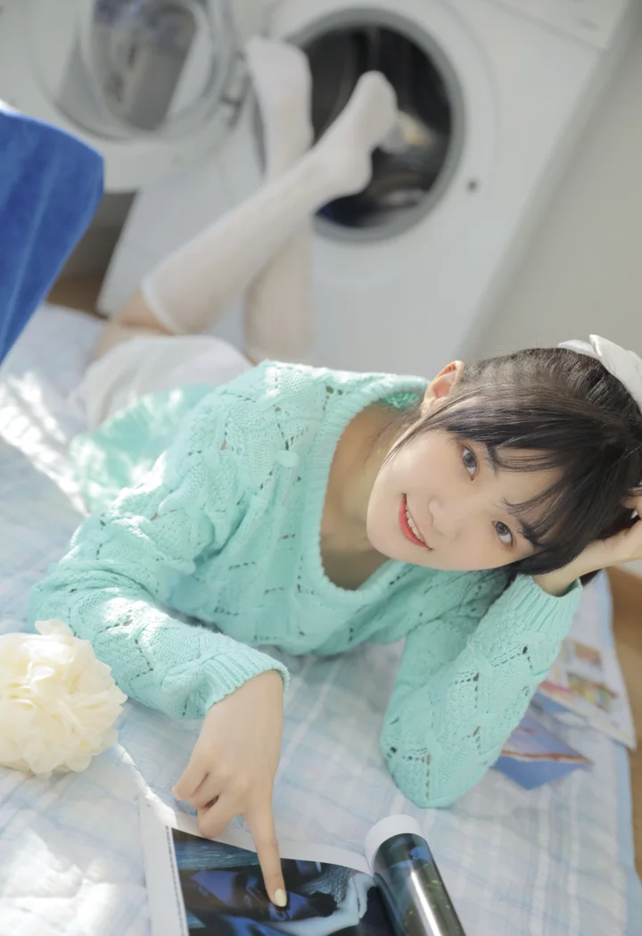 一名女子穿着薄荷色针织毛衣躺在床上翻看杂志。