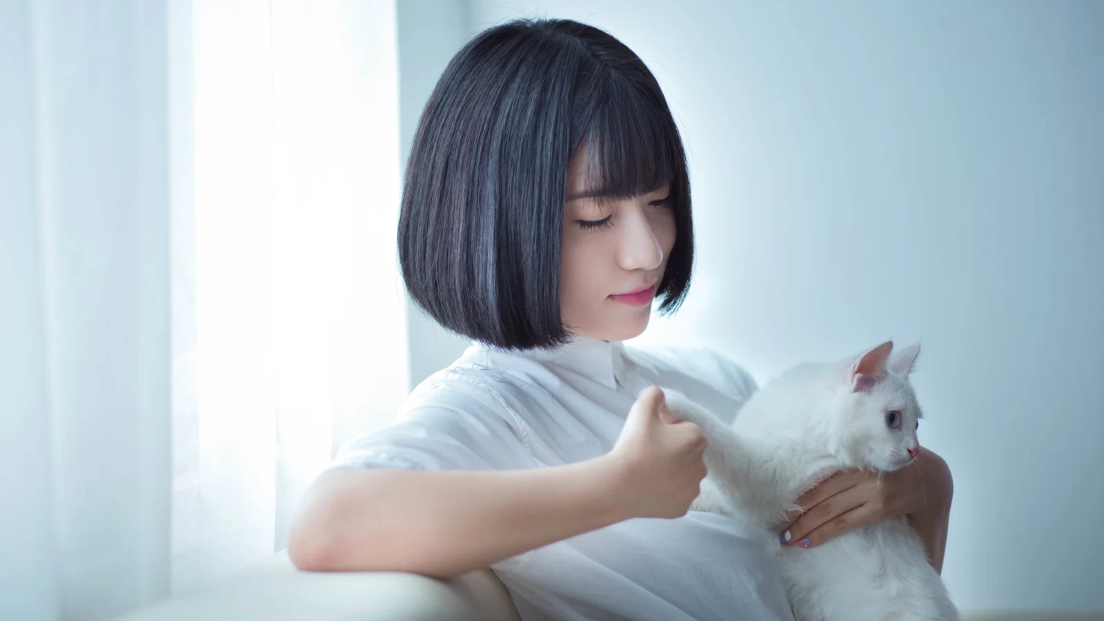 一名短髮女子抱著一隻白貓，置身於明亮柔和的室內光線中。