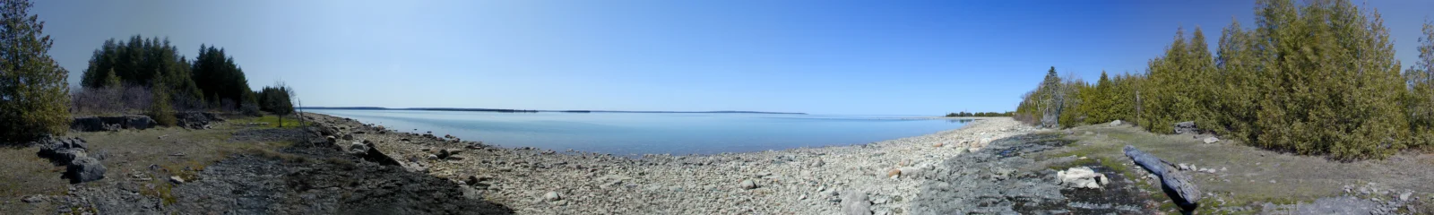 蓝天下的湖岸延伸至远方，岸边遍布岩石与树木。