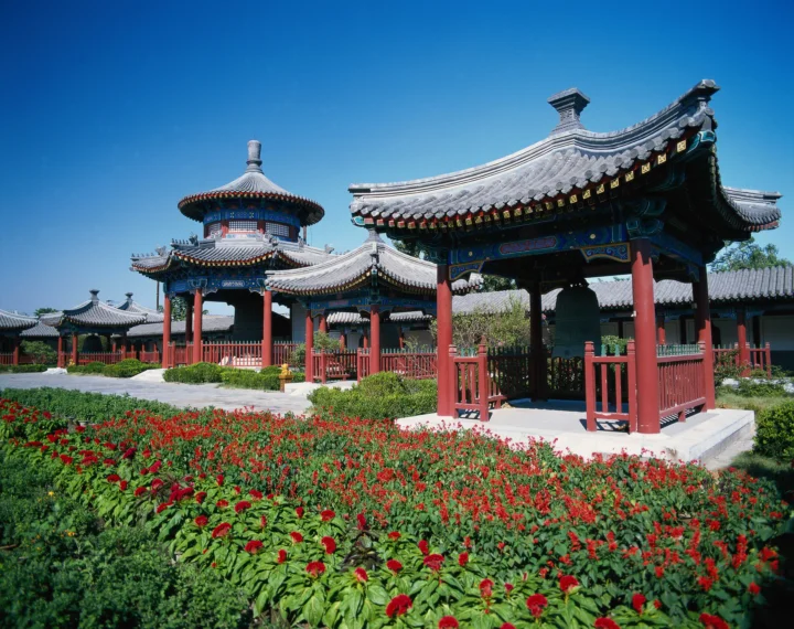 蓝天下的中式园林中坐落着 ornamented亭阁，前景盛开着大片红色花卉。