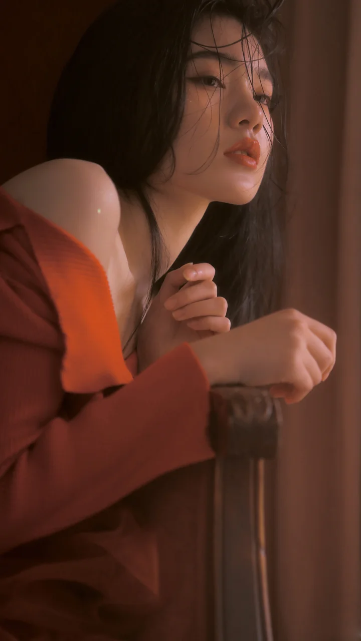 一名成年女性身穿红色针织衫，在暖色室内光线下侧身凝视镜头。