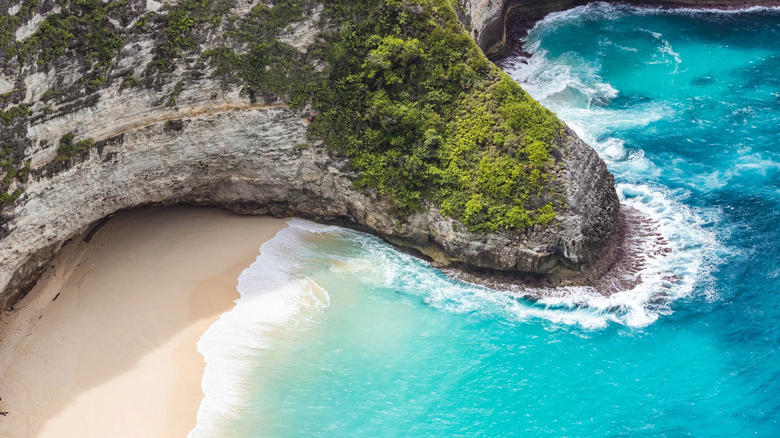 岩石悬崖环抱着一处沙滩海湾，碧 turquoise 的海水拍打着岸边。