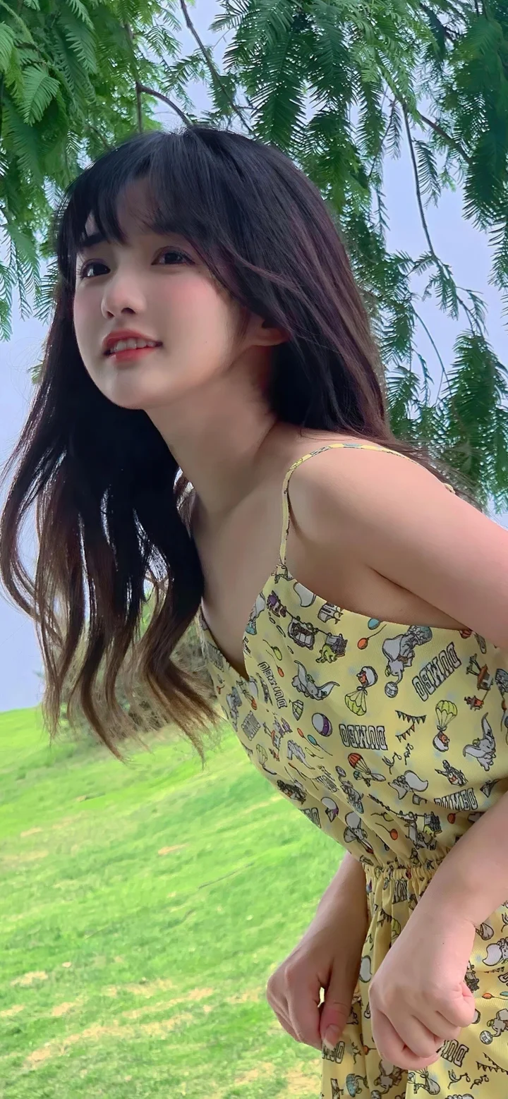 一名长发女性在绿树和草地环绕的户外环境中侧身看向镜头。