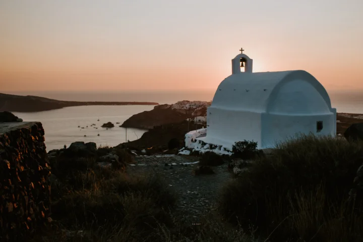 暮色中的白色圆顶教堂坐落在海岸边，远处海面映着柔和的夕阳。