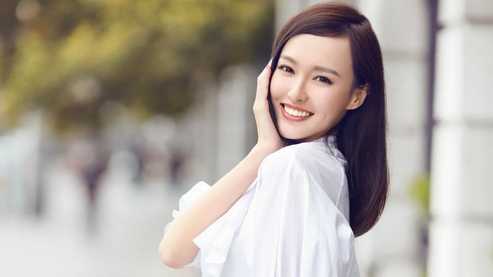 一名身穿白色上衣的成年女性在户外微笑回望镜头。