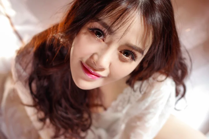 갈색 긴 머리의 여성이 흰색 상의를 입고 미소 짓는 근접 인물 사진입니다.