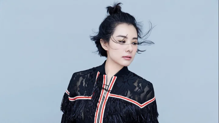 一名成年女性身穿黑色流苏服饰站在浅蓝灰色背景前。