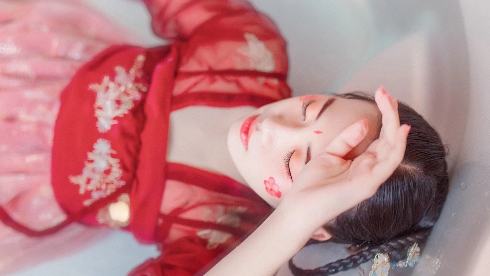 一名身穿红色传统服饰的女子闭眼侧卧，并用手遮在额前。