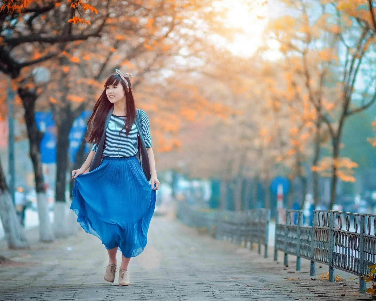 一名身穿蓝色裙子的女子走在秋叶环绕的公园小路上。