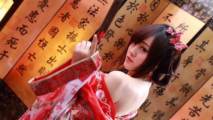 一名身穿红色传统服饰的成年女子站在书法背景前。