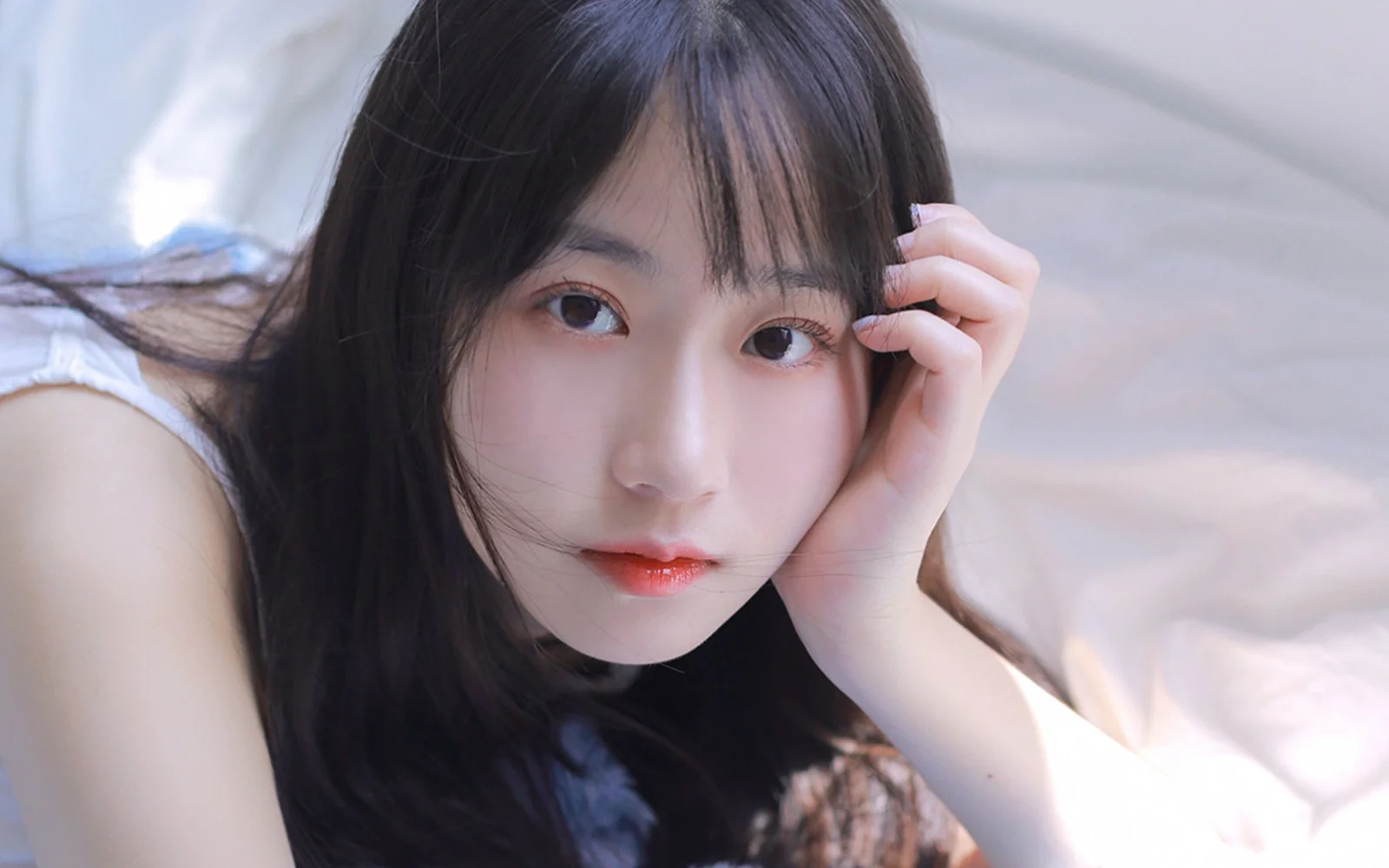 一名黑发女子在柔和光线下托腮直视镜头。