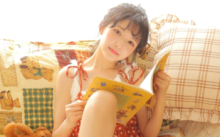 一名女性坐在床上阅读一本彩色书籍。