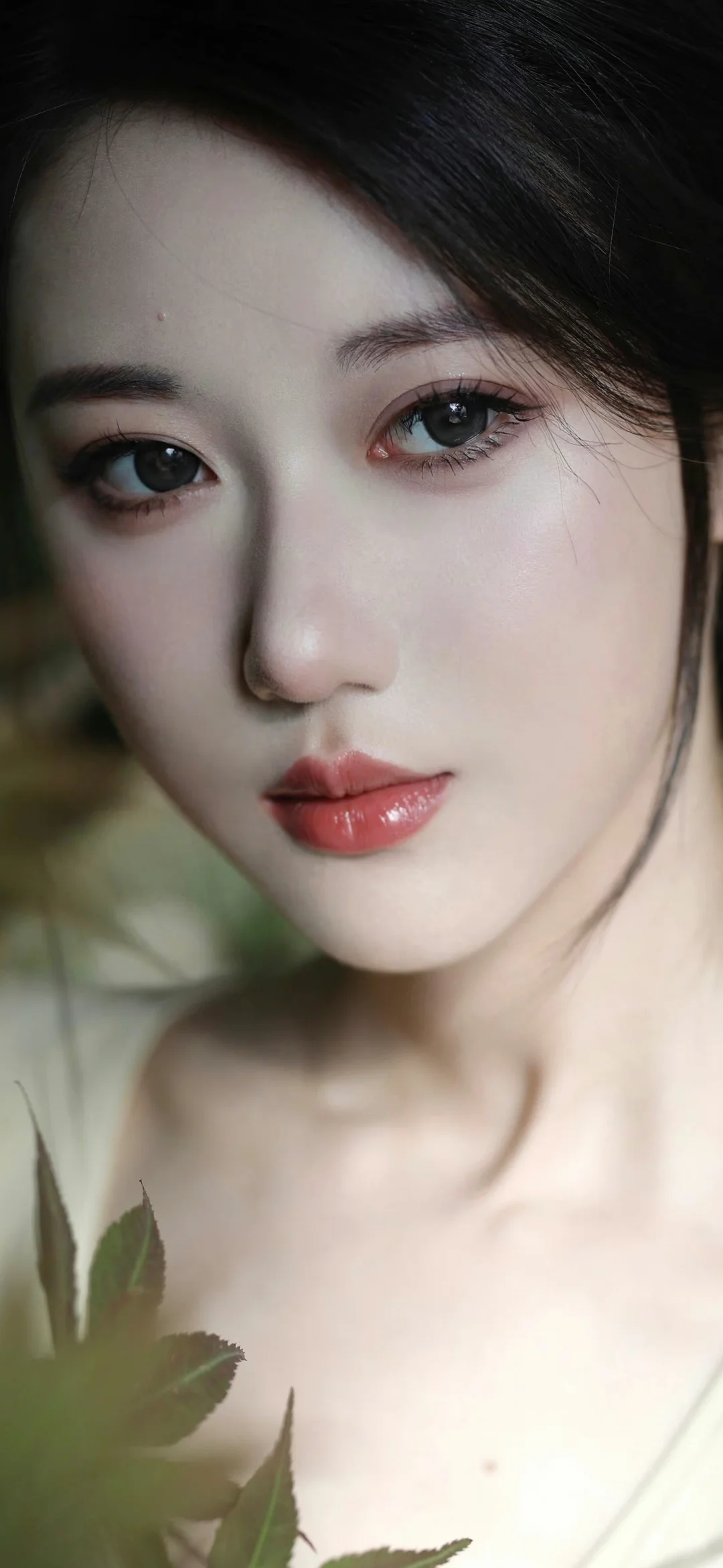 一位成年女性的近距离肖像，柔和光线映照着她的面容，前景带有虚化的绿色植物。