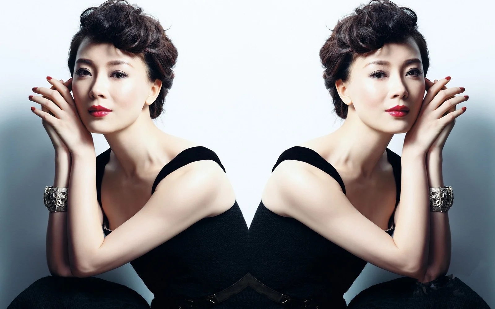 画面中一位身穿黑色连衣裙的成年女性以镜像构图面对镜头，背景为浅灰色。
