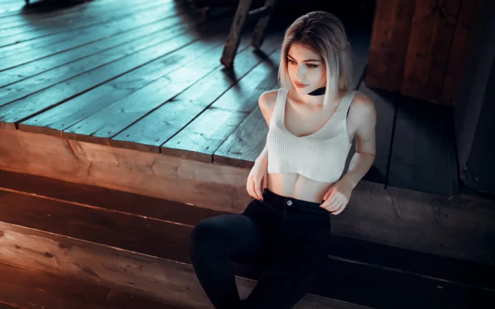 一名成年女性坐在木质室内空间中，穿着白色短款上衣和黑色长裤。