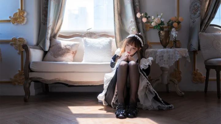 一名身穿黑白服装的女性坐在华丽室内的地板上，窗边阳光洒落在她身旁。