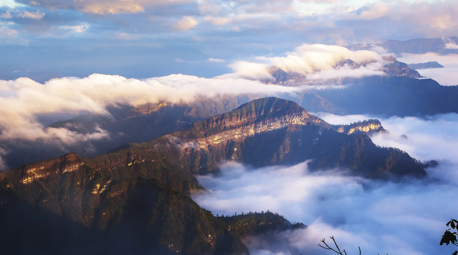 山々が雲海と柔らかな光の中に連なり、壮大な高地の風景を映し出している。