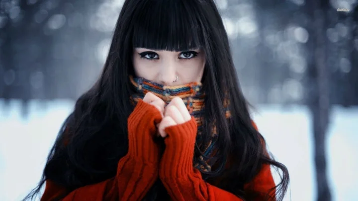 一名长发女子在雪地中用红色围巾遮住下半张脸。