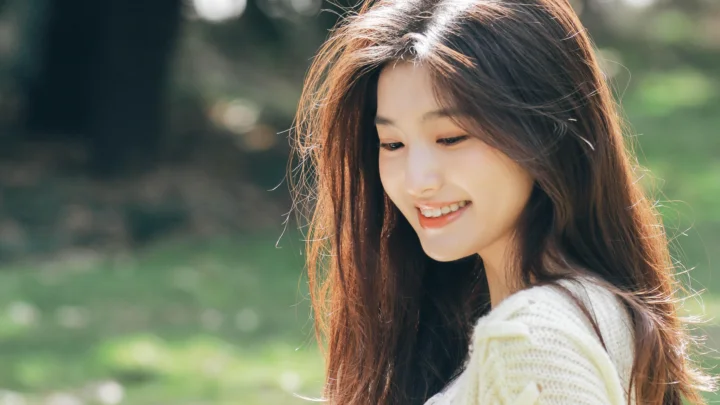 긴 머리의 여성이 야외 햇살 속에서 뒤돌아보며 미소 짓고 있다.