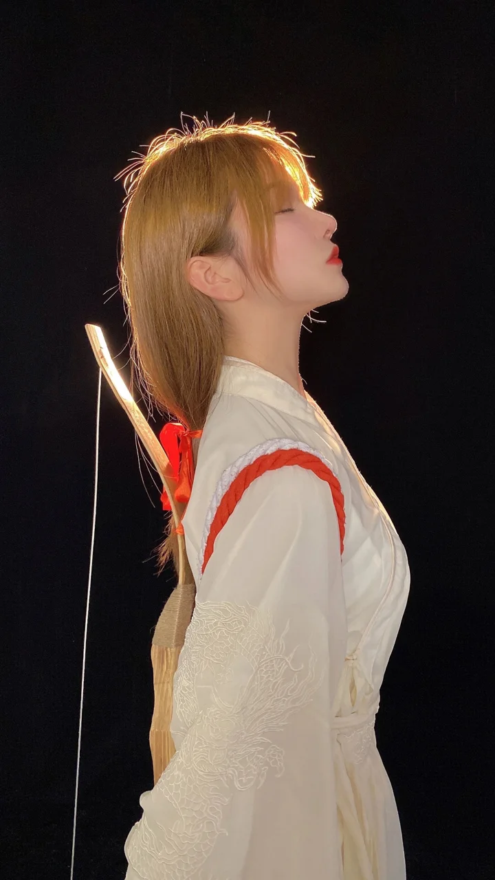 一名成年女性身穿白色传统服饰，在黑色背景前呈侧身姿态。