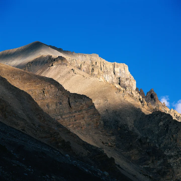 阳光照亮的高山岩壁在深蓝天空下展现出鲜明的层理与阴影。