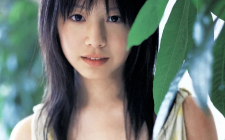 一名女性在绿叶间面对镜头，画面以她的脸部和上半身为主。