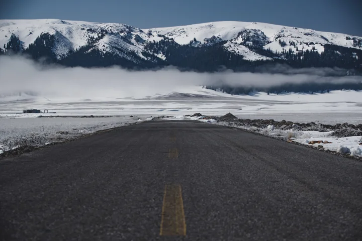 一条公路通向被雾气环绕的白雪山脉，远处点缀着深色针叶林。