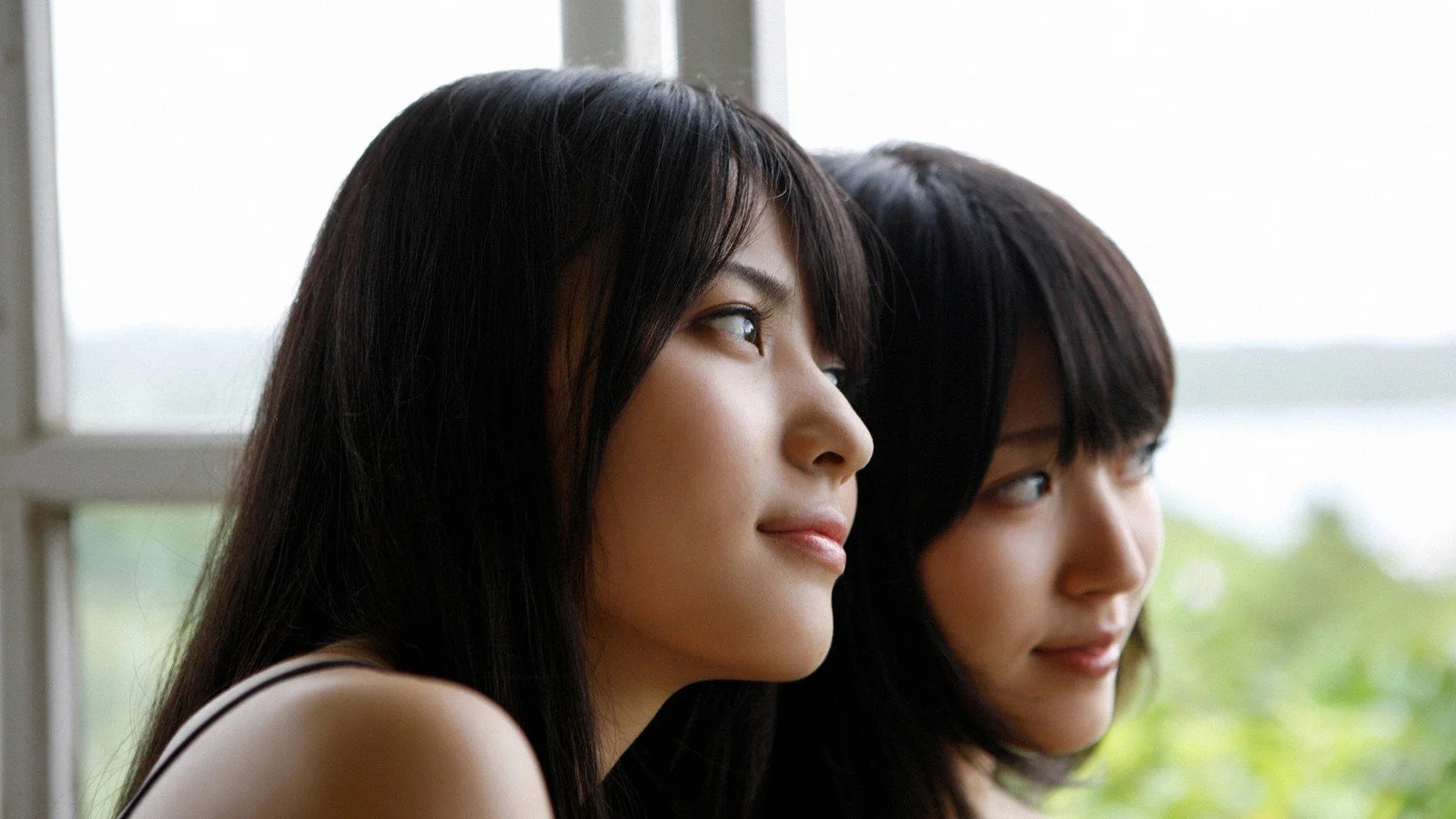 二人の黒髪の女性が窓辺に並び、横顔で外を見つめている。