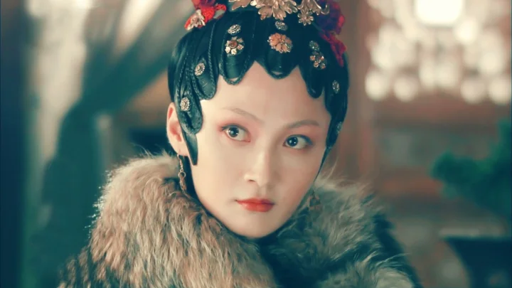 화려한 전통 머리 장식과 털 깃을 착용한 여성이 부드럽게 흐려진 실내를 배경으로 클로즈업되어 있습니다.