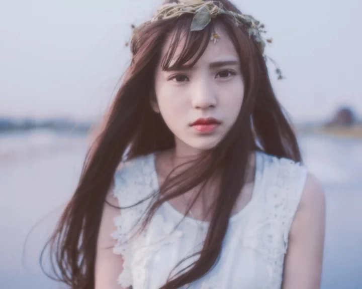 一名戴着花冠、留着长发的女子站在水边。