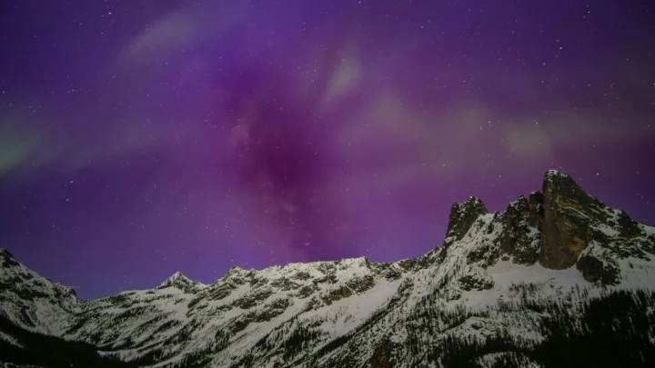 紫色星空和银河横跨雪覆盖的锯齿山峰上方。