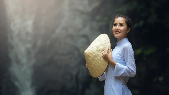 一名身穿白色衣服的女子在户外手持一顶锥形草帽。