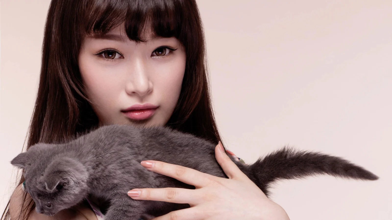 긴 머리의 여성이 카메라를 바라보며 회색 고양이를 안고 있다.
