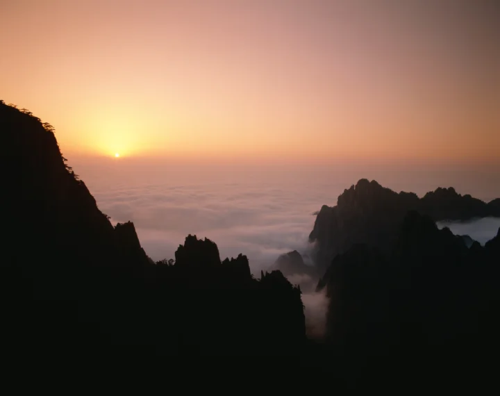 夕阳映照着云海，群山以深色剪影呈现在暖色天空下。