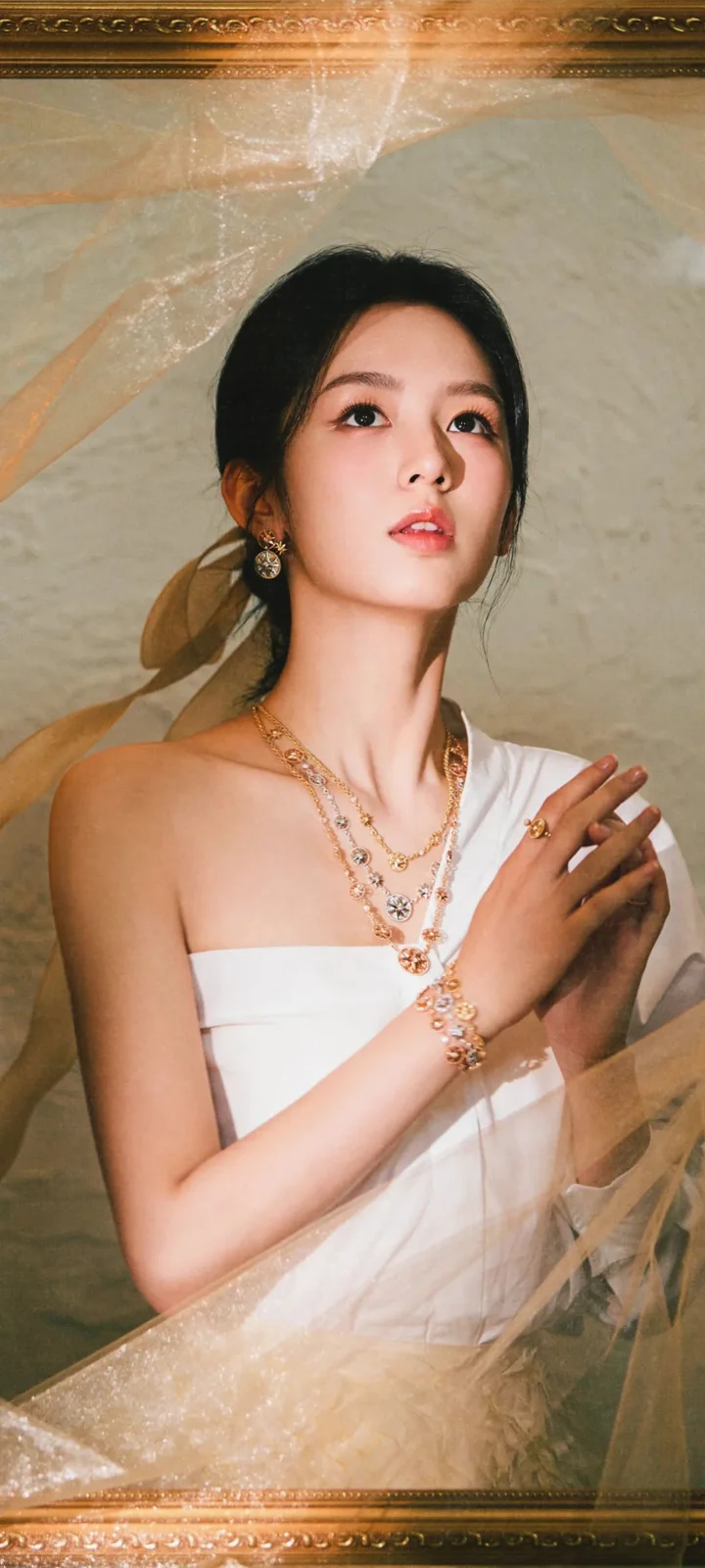 一位穿白色礼服、佩戴多层项链和耳饰的女性站在浅色背景前。