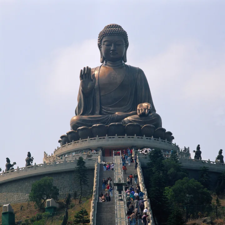一尊巨大的佛像坐落在寺庙平台上方，前方是石阶和游客。