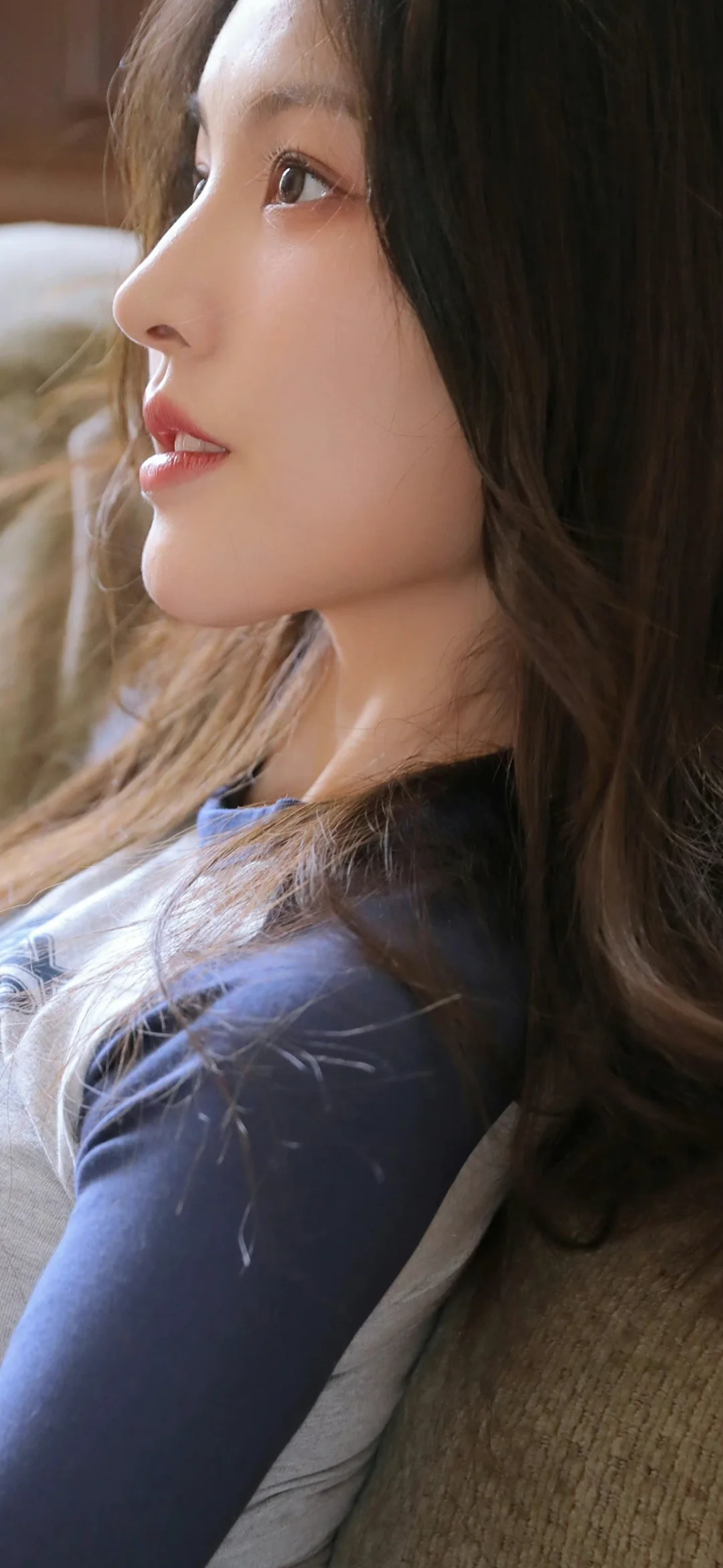 一位长发女性身穿深色上衣，呈侧脸近景。